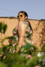 A woman standing to the side outdoors in sunglasses wearing the cotton Tropicana Dress in the hand batiked print Waters.
