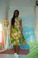 A person wearing a vibrant green and pink floral dress, standing against a backdrop of an unfinished painted mural.